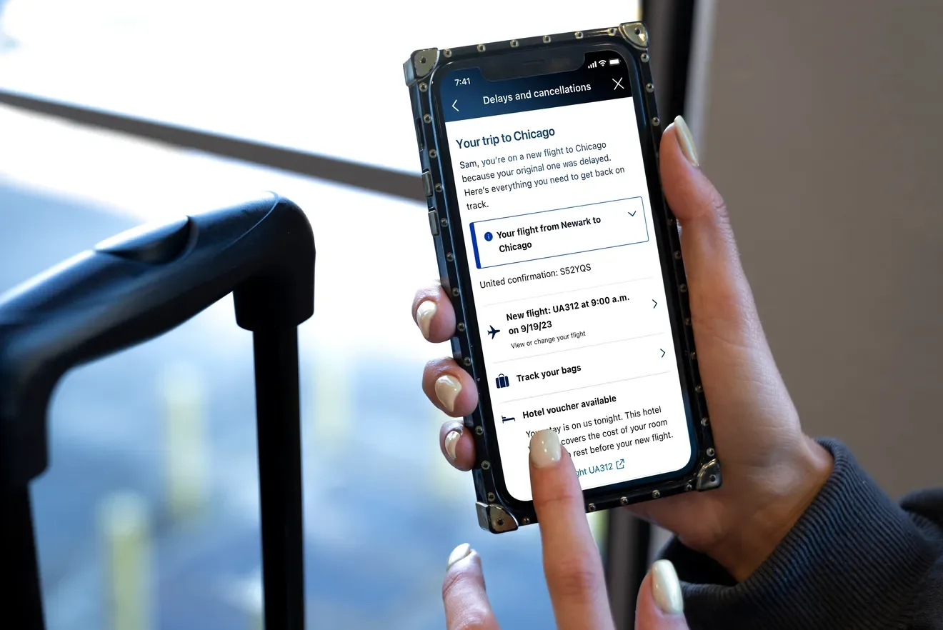 A person holds a smartphone with the United app displayed, giving context for their delayed flight. AI airline systems like automated messaging help passengers understand delays and curb frustrations.